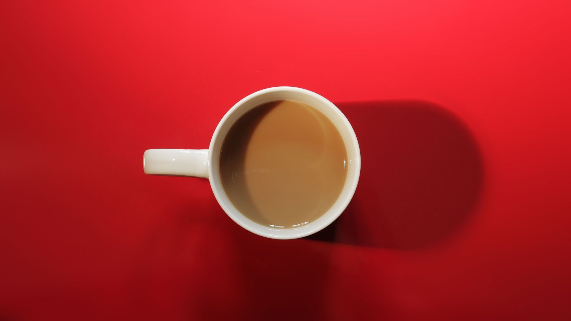 Top-down view of a white coffee mug on a bright red background
